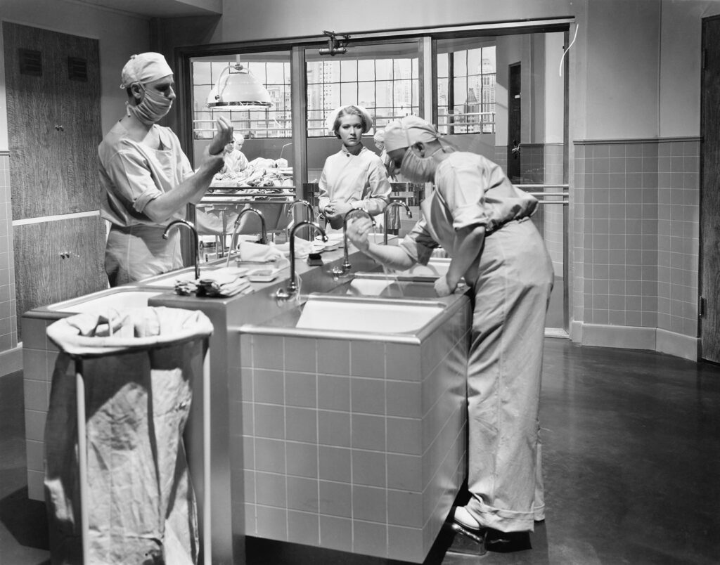 Two surgeons and a nurse washing and gloving their hands to prepare for an operation