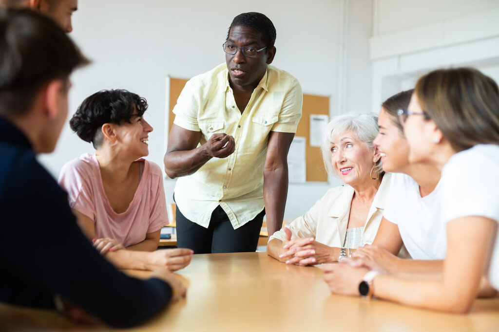 A standing individual speaking to a group seated around a table