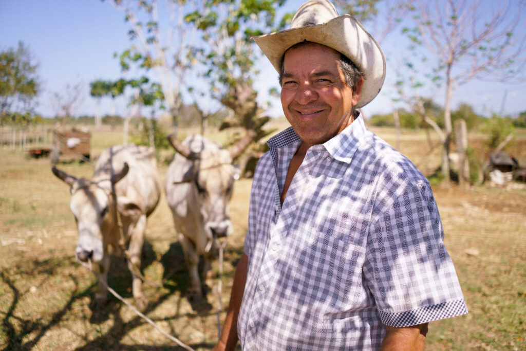 Farmer smiles to the camera with his two oxen in the background.
