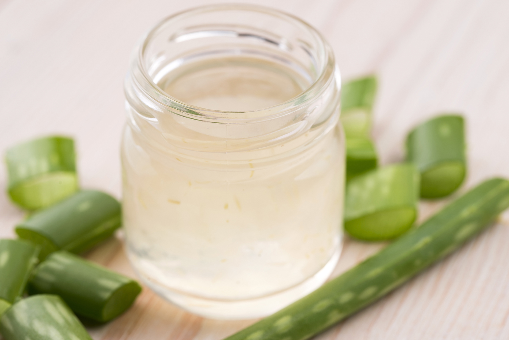 A jar of aloe vera juice with fresh aloe leaves on the surface next to the jar