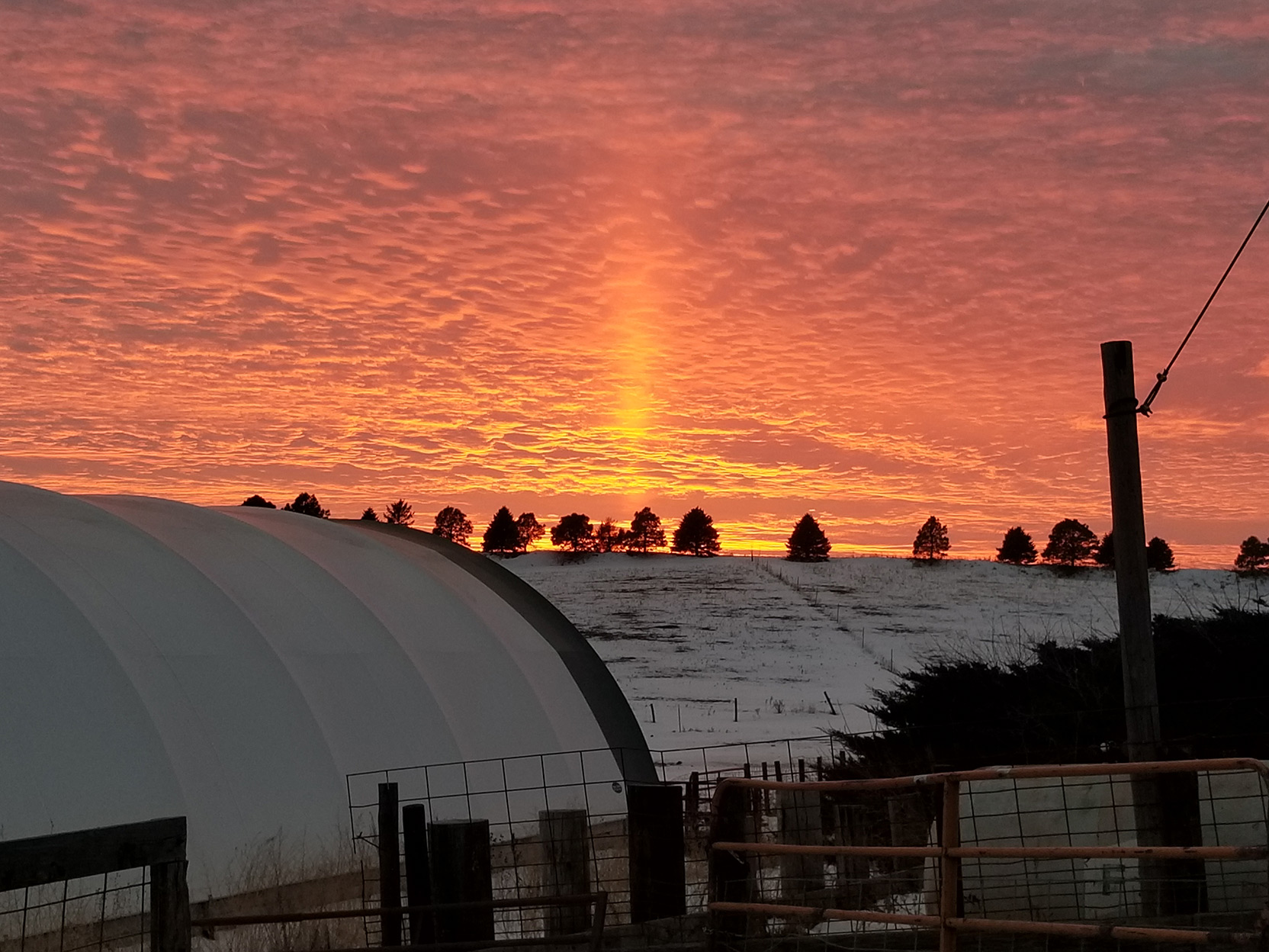 A hoop barn in a snow covered field with a sunset in the background